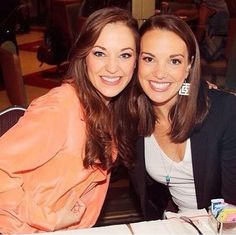 two women sitting at a table posing for the camera with their arms around each other