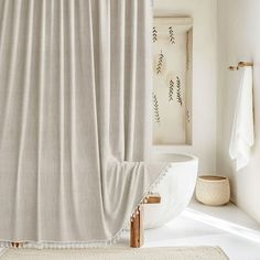 a white bath tub sitting next to a window covered in a beige shower curtain and rug