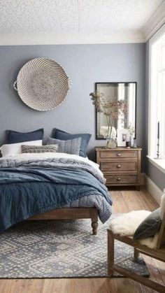 a bedroom with blue walls and wooden flooring, a round mirror above the bed