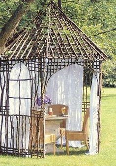 an outdoor gazebo made out of sticks and branches with a table in the middle