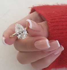 a woman's hand holding a ring with a pear shaped diamond on it, in front of a red sweater