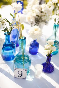 blue vases with white flowers are sitting on a table number 9, which is placed next to each other