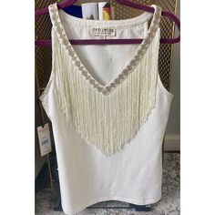 a white top with fringes hanging on a rack