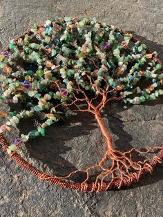 a tree with many beads on it sitting on top of a stone slab in front of a rock