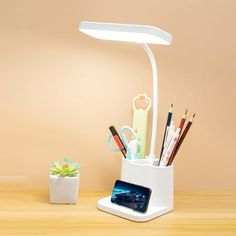 a desk lamp with pens, pencils and other office supplies in it on a wooden table