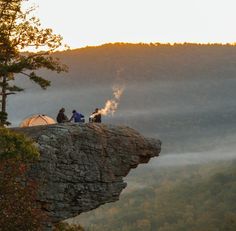 three people sitting on top of a cliff with a tent