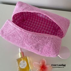 a pink cosmetic bag next to a bottle of perfume on a white table with flowers