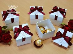 six white boxes with red ribbons and chocolates in them sitting on a wooden table