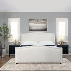 a white bed sitting on top of a wooden floor next to two windows in a bedroom