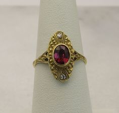 a close up of a ring with a red stone in it on a white surface