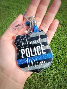 a hand holding a police mom keychain on top of a green grass covered field