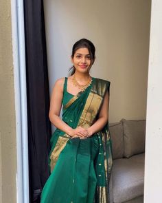 a woman in a green and gold sari standing next to a couch with her hands on her hips