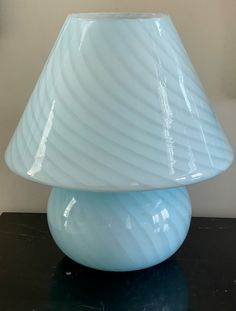 a light blue vase sitting on top of a black table next to a white wall