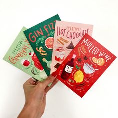 hand holding four christmas greeting cards in front of white background with text that reads gin fizz, hot chocolate, nutted wine and festive