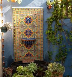 an outdoor fountain surrounded by potted plants and other greenery in front of a blue wall