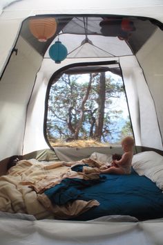 a baby is sitting on a bed in a tent with the window open to look outside