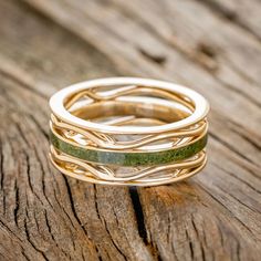 three gold rings with green and white stones on top of each other, sitting on a piece of wood