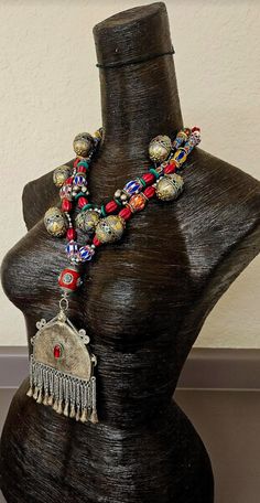 Here's a gorgeous, wild and exotic tribal or ethnic beaded statement necklace - chest piece from my private vault. New and unworn. The vintage pendant, which measures 4.5" x 3.75" is from the Middle East, etched and has a piece of red inlaid glass to ward off the "evil eye." All of the attached dangles are intact which is rare for pieces of this age and genre. A double strand necklace supports the pendant and features the following components: chevron beads, red oval "squash" beads, shiny silver balls, African hand painted glass, bone, ornate metal Turkman beads with possible inlaid gemstones, turquoise slices, gold tone metal wavy potato chip spacers, tiny silver tone vintage bells and a large red Tibetan resin inlaid focal bead. This lightweight piece adjusts from 19-22" and is finished Bohemian Beads For Traditional Ceremonies And Festivals, Bohemian Handmade Beaded Necklaces For Traditional Ceremonies, Bohemian Jewelry With Large Beads For Traditional Ceremonies, Multicolor Bohemian Necklaces For Traditional Ceremonies, Red Bohemian Necklaces For Traditional Ceremonies, Bohemian Red Necklaces For Traditional Ceremonies, Bohemian Beaded Necklaces For Traditional Ceremonies, Bohemian Multicolor Necklaces For Traditional Ceremonies, Bohemian Ceremonial Necklaces With Polished Beads