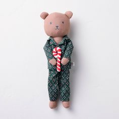 a teddy bear wearing pajamas and holding a candy cane in his hands, against a white wall