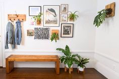 a wooden bench sitting in front of a white wall with pictures on it and potted plants