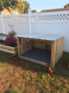 a dog house made out of wooden pallets in the yard with flowers around it