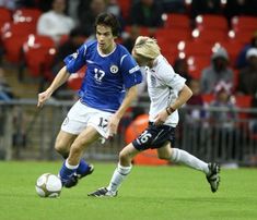 two men playing soccer on a field with fans in the bleachers behind them