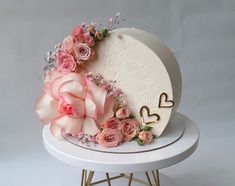 a white cake with pink flowers and hearts on the top is sitting on a stand