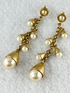 Satin gold tone and elegant. Each earrings has 4 small pearls and a final larger pearl at the bottom. In excellent condition. Vintage Gold Earrings With Pearl Charm, Gold-tone Pearl Drop Dangle Earrings, Classic Gold Metal Pearl Earrings, Gold Pearl Earrings With Dangling Beads For Party, Formal Gold Pearl Drop Clip-on Earrings, Gold-tone Dangle Earrings With Pearl Drop, Elegant Gold-tone Dangle Clip-on Earrings, Evening Pearl Drop Dangle Clip-on Earrings, Gold Dangle Pearl Earrings For Formal Occasions