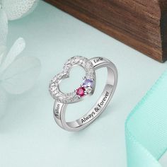 two heart shaped rings with names engraved on the sides and hearts in the middle, sitting next to a flower