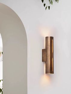 a wall light mounted on the side of a white wall next to a potted plant