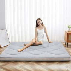 a woman sitting on top of a mattress in the middle of a room with white curtains