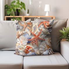 a pillow with shells and starfishs on it sitting on a couch next to a potted plant