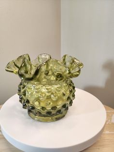 a green glass vase sitting on top of a white plate next to a lamp shade