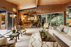 a living room filled with lots of furniture next to a window covered in wood paneling