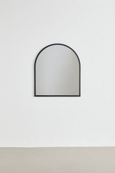 a white wall with a black arched mirror on it's side and a light gray floor