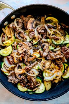 a skillet filled with meat, onions and zucchini slices on top of a table