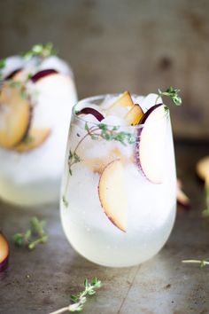 two glasses filled with ice and fruit on top of a wooden table next to sliced apples