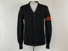 "Vintage 1940s letterman school cardigan sweater. Made of black knit wool with orange stripes on left arm. Has a six button front and two pockets. Has owner's name ART KRELLWITZ embroidered on patch inside. Made by NELSON KNITTED MILLS DULUTH, MINN. About a size small. Actual measurements are:   39\" around the chest   37\" around the waist   18.5\" shoulder seam to shoulder seam   27\" shoulder seam to end of cuff, uncuffed  27\" overall length   4\" banded cuffs In very good condition." Vintage Black Cardigan With Button Closure, Black Retro Cotton Cardigan, Vintage Black Sweater With Buttons, Black Vintage Cardigan For Fall, Vintage Wool Sweater For Workwear, Vintage Workwear Sweater With Button Closure, Vintage Sweater With Button Closure For Work, 1940s Sweater, School Cardigan