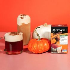 two pumpkins, an iced drink and a box of stash coffee on a pink table