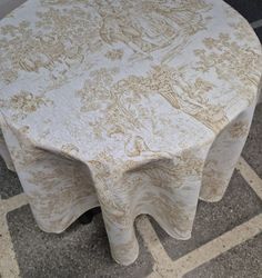 a round table with a white and gold design on it's top, sitting in front of a brick wall