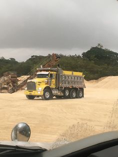 a yellow dump truck driving down a dirt road