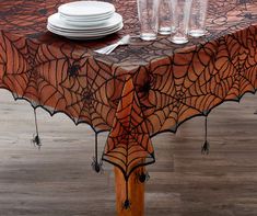 a spider web tablecloth with white plates and silverware on the top, sitting on a wooden table