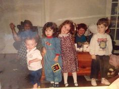 a group of children standing next to each other in front of a dresser and window