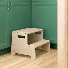 a wooden step stool sitting in front of green cabinets