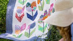 a woman with a hat is looking at a colorful quilt on the grass in front of her