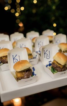 small trays filled with mini hamburgers sitting on top of a white table next to a christmas tree