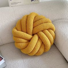 a yellow knot on the back of a white couch next to a book and phone