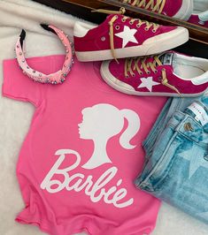 a pink shirt with the word barbie on it next to two pairs of jeans and sneakers