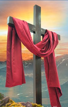 a cross with a red cloth draped around it and mountains in the background at sunset