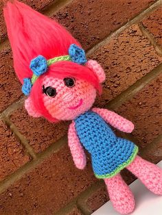 a crocheted doll with pink hair and blue dress sitting against a brick wall